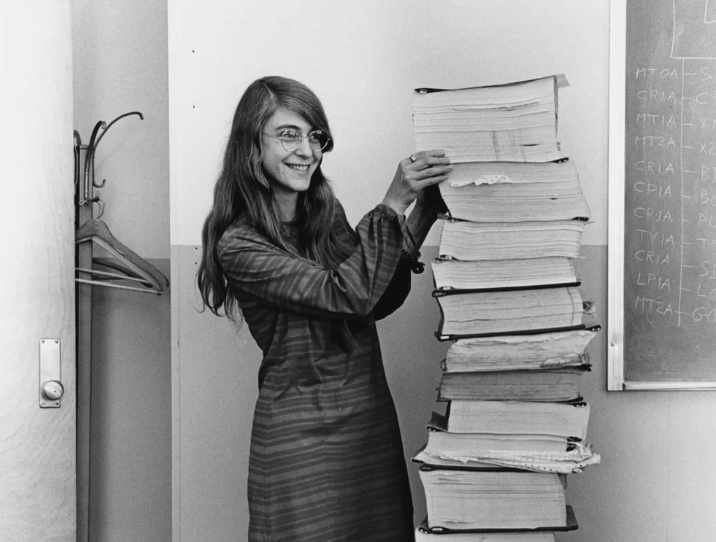 Margaret Hamilton standing beside printouts of the Apollo guidance computer source code